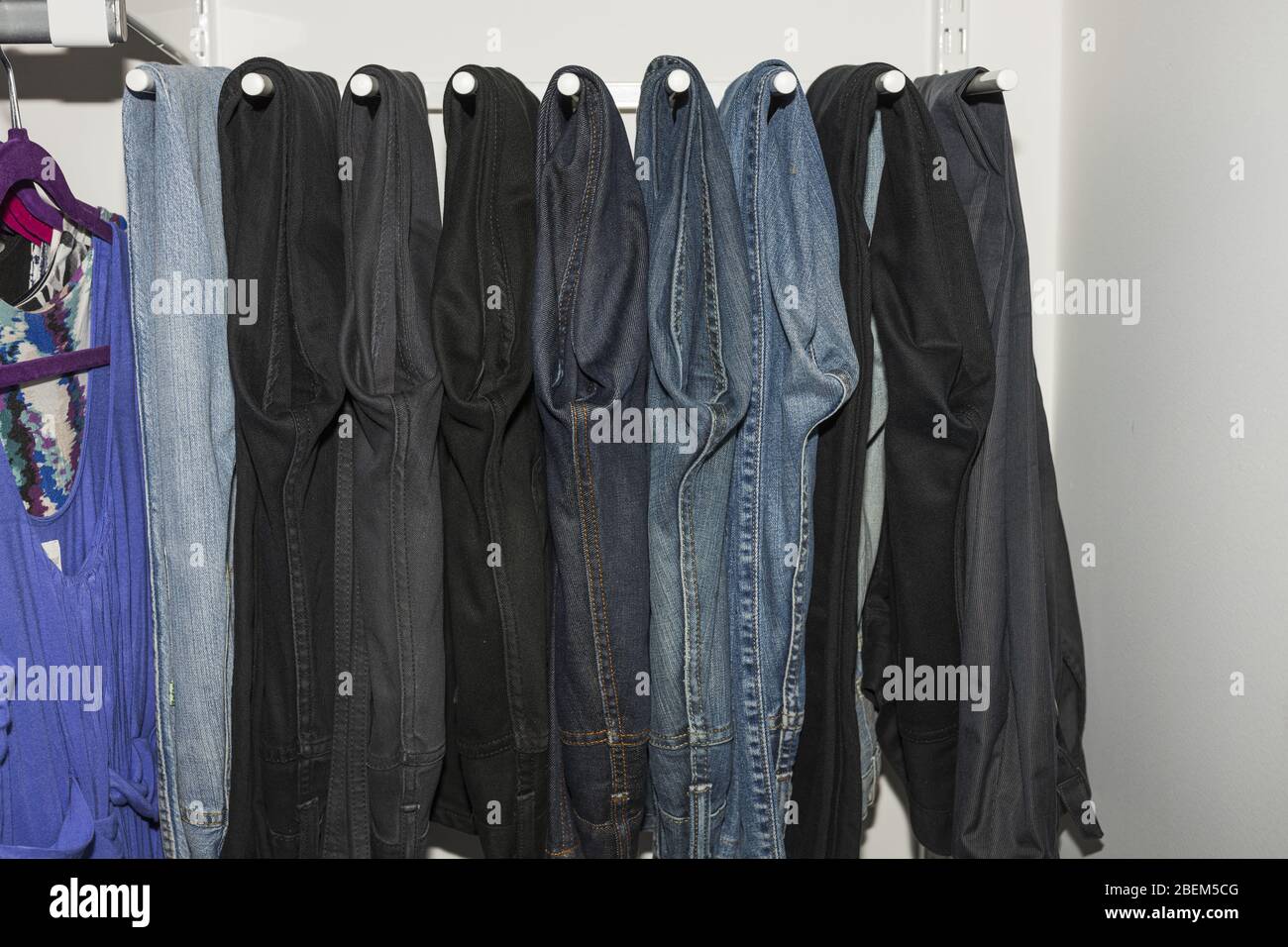 Close up view of interior of built-in wardrobe. Blue and black jeans on white hangers. Cloth organizer. Stock Photo