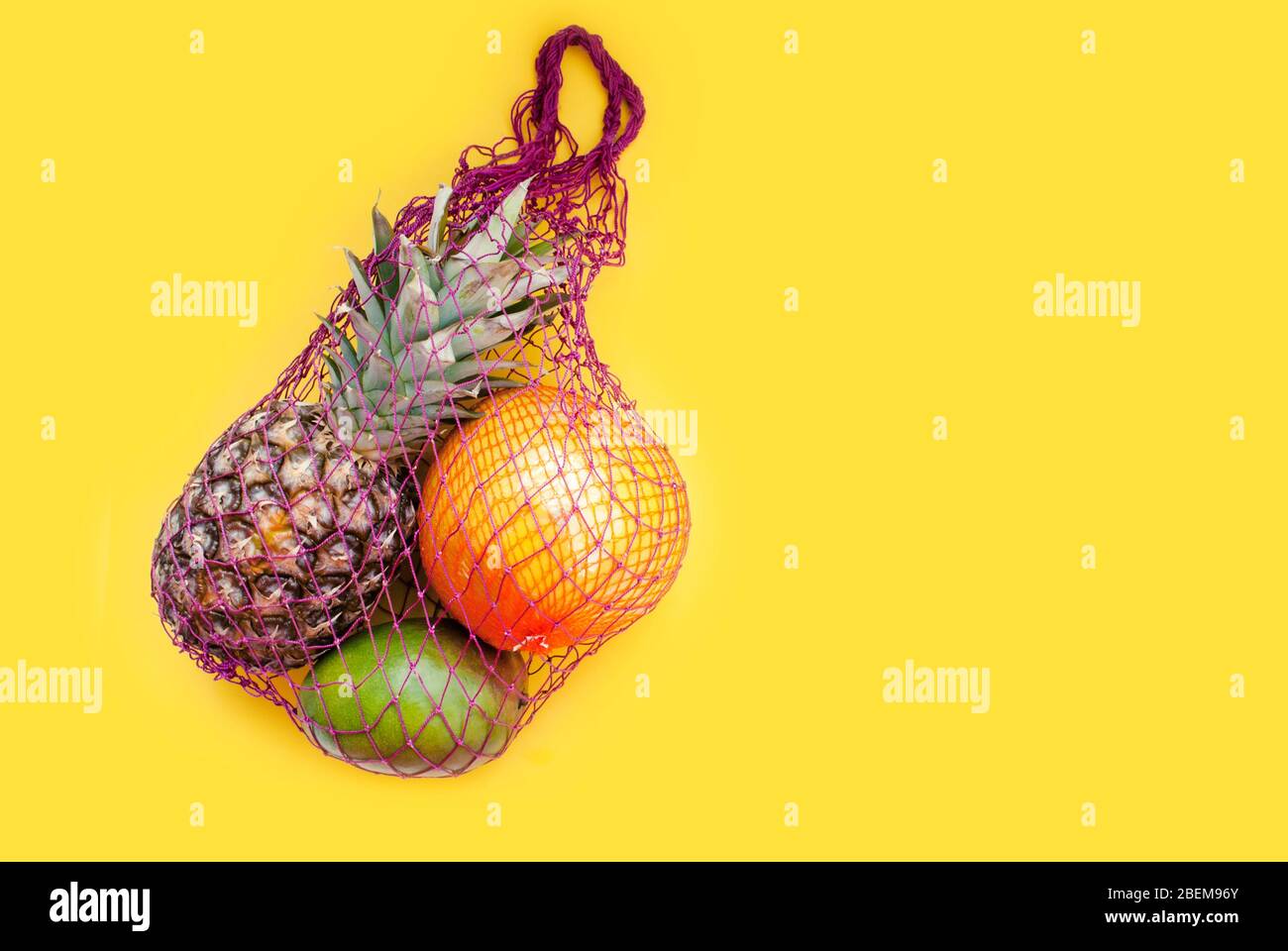 https://c8.alamy.com/comp/2BEM96Y/tropical-fruits-in-a-string-string-bag-pineapple-mango-pomelo-yellow-background-place-for-text-2BEM96Y.jpg