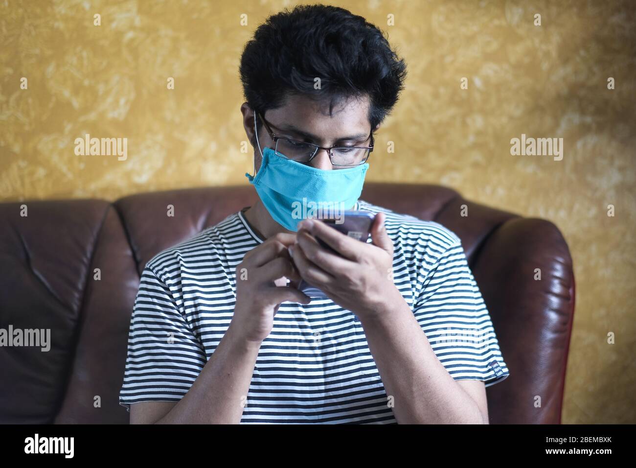 man using smartphone while wearing surgical mask indoor . Stock Photo