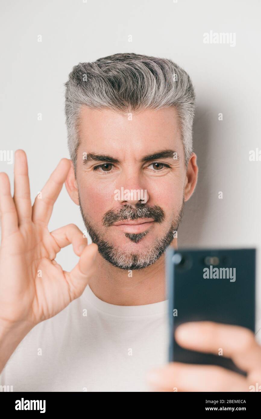 Caucasian young man with white hair and beard smiles and makes a gesture of  everything perfect with his hand, while making a video call with his mobil  Stock Photo - Alamy