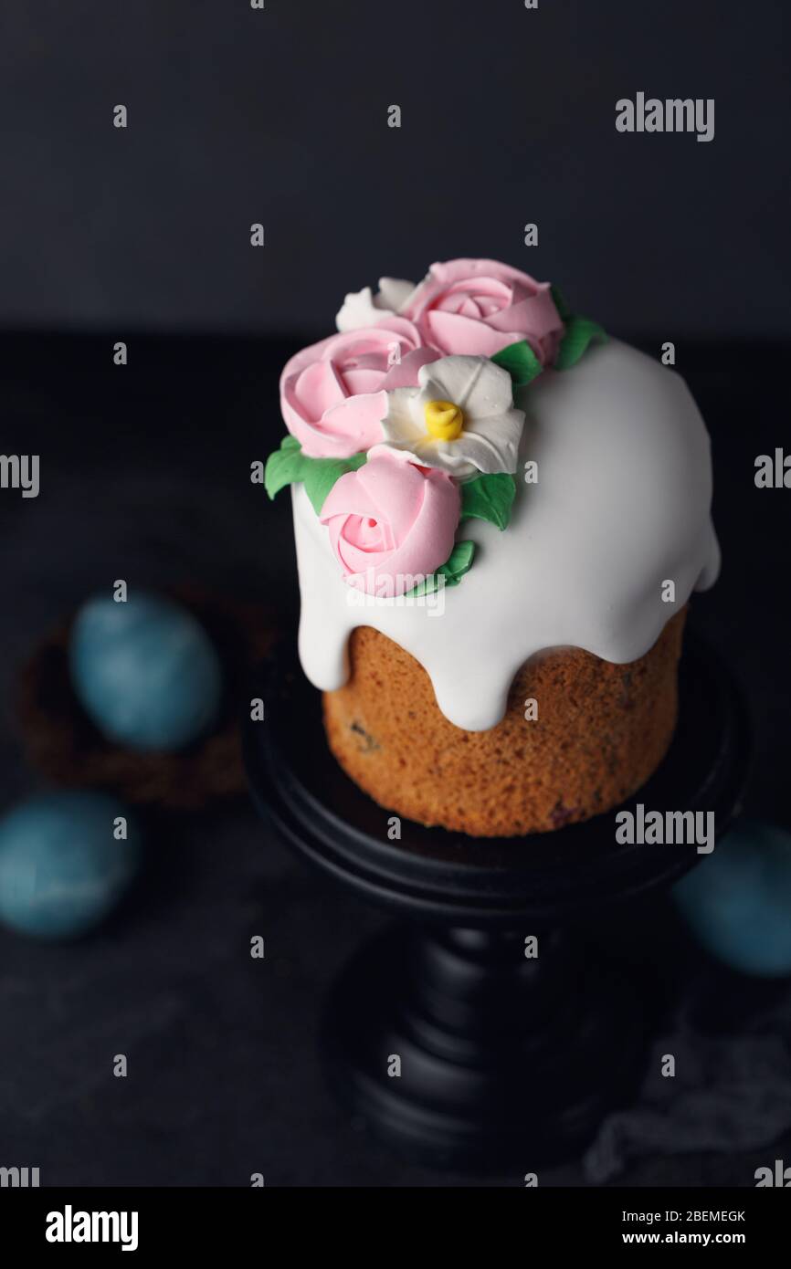 Easter cake with pink creamy roses on wooden black stand on dark grey textured background. Holiday concept. Easter inspiration. Copy space Stock Photo
