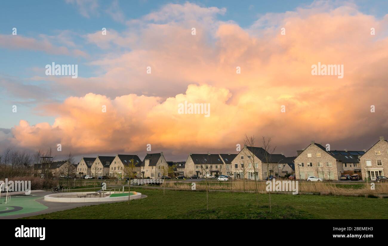 Rain shower is beautifully illuminated by the light of the setting sun. Residential buildings in cottage style of new housing estate in a dutch town. Stock Photo