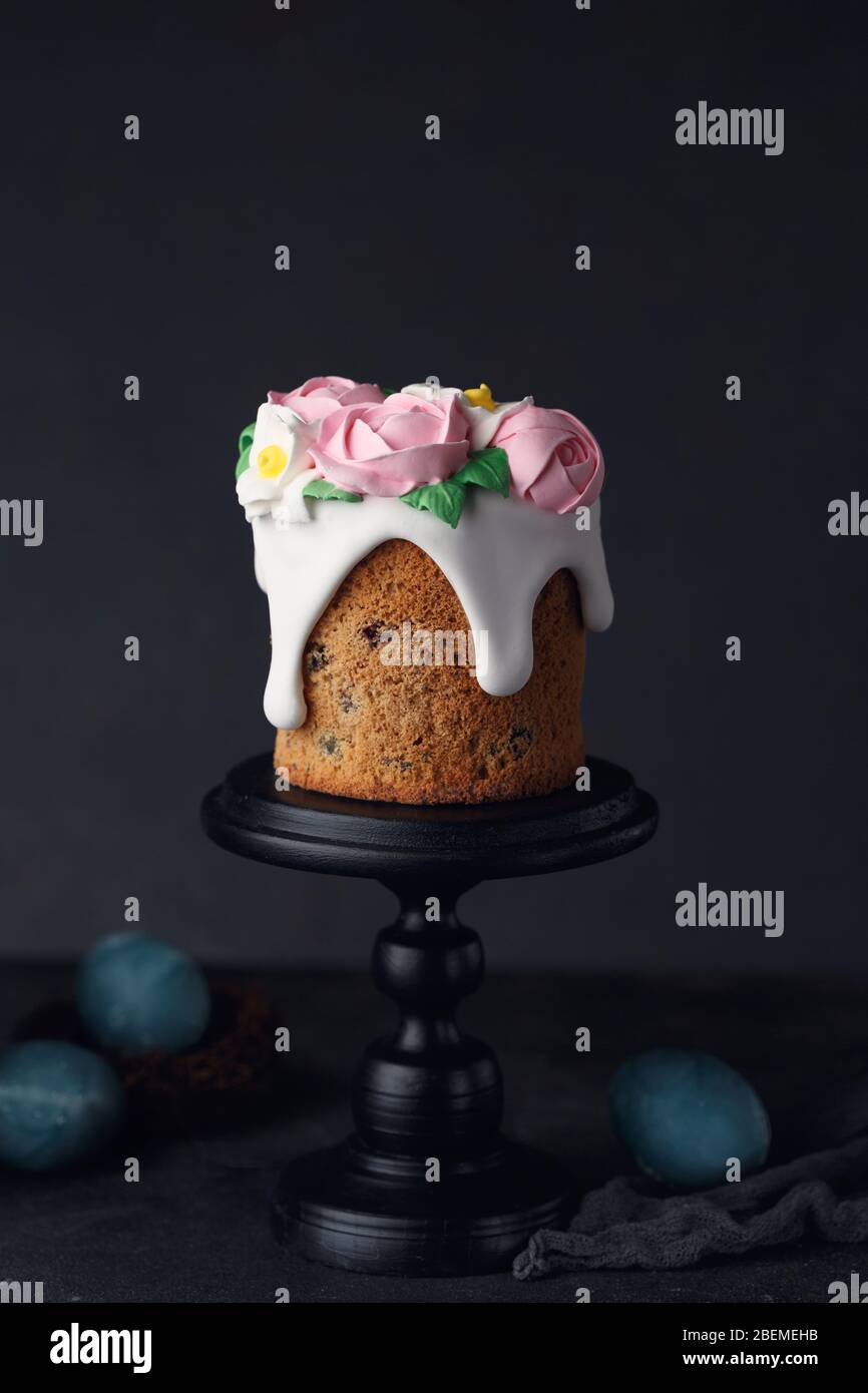 Easter cake with pink creamy roses on wooden black stand on dark grey textured background. Holiday concept. Easter inspiration. Copy space Stock Photo