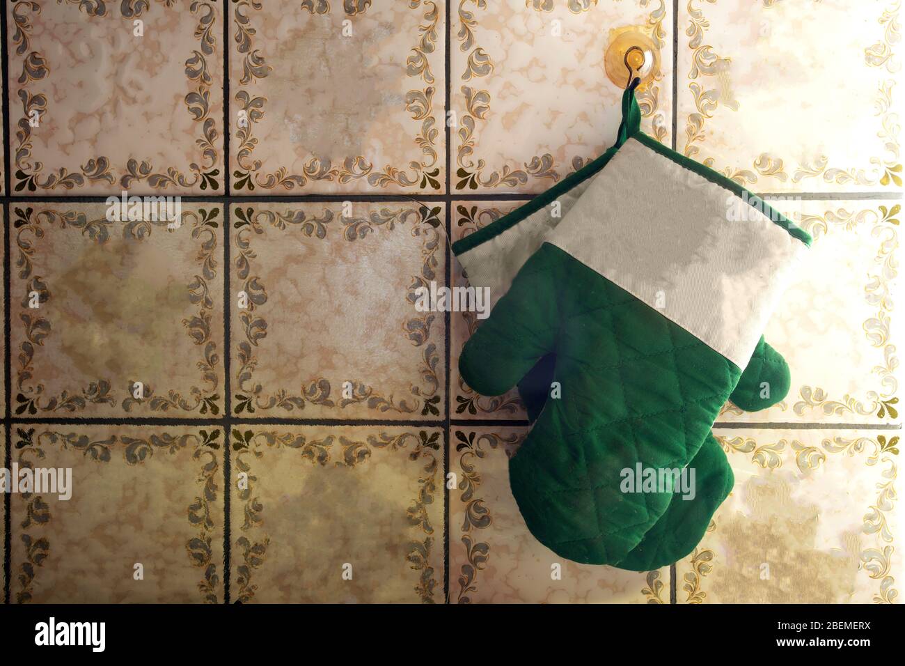 Green oven mitts hang on old-fashioned wall with pattern tiles antique design Stock Photo