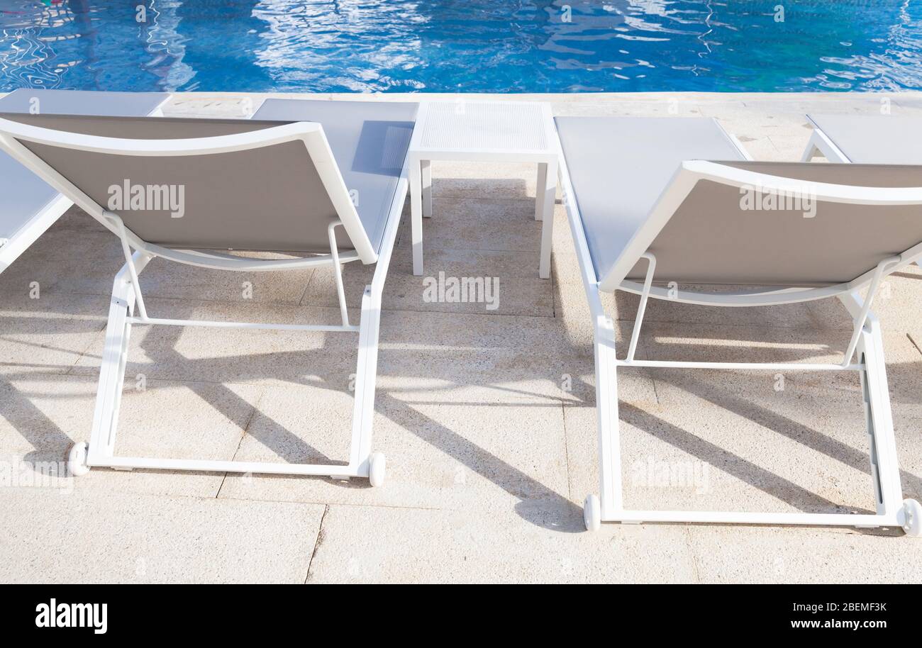 Vacant white sunloungers by a swimming pool Stock Photo