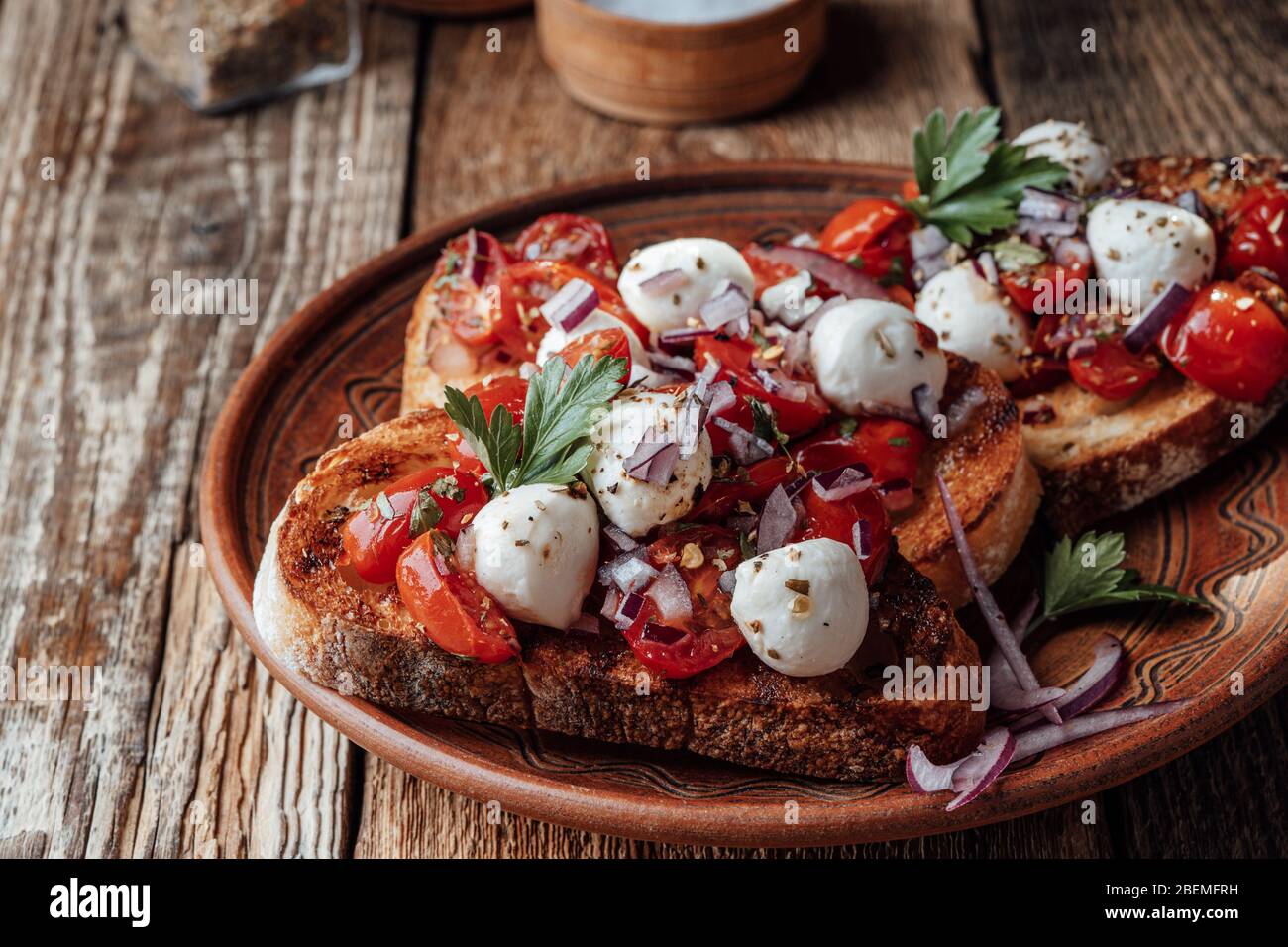 Tomato bruschetta with mozzarella and herbs in rural ceramic bowl, close up Stock Photo