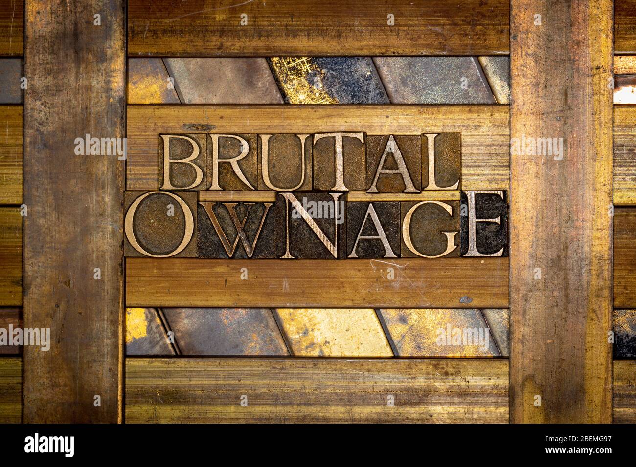 Photo of real authentic typeset letters forming Brutal Ownage text on vintage textured grunge copper and gold background Stock Photo