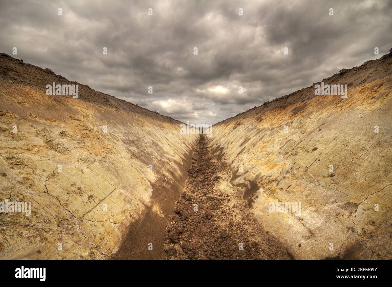 Freshly dug field drainage ditch showing soil stratification under a sky with dark clouds Stock Photo