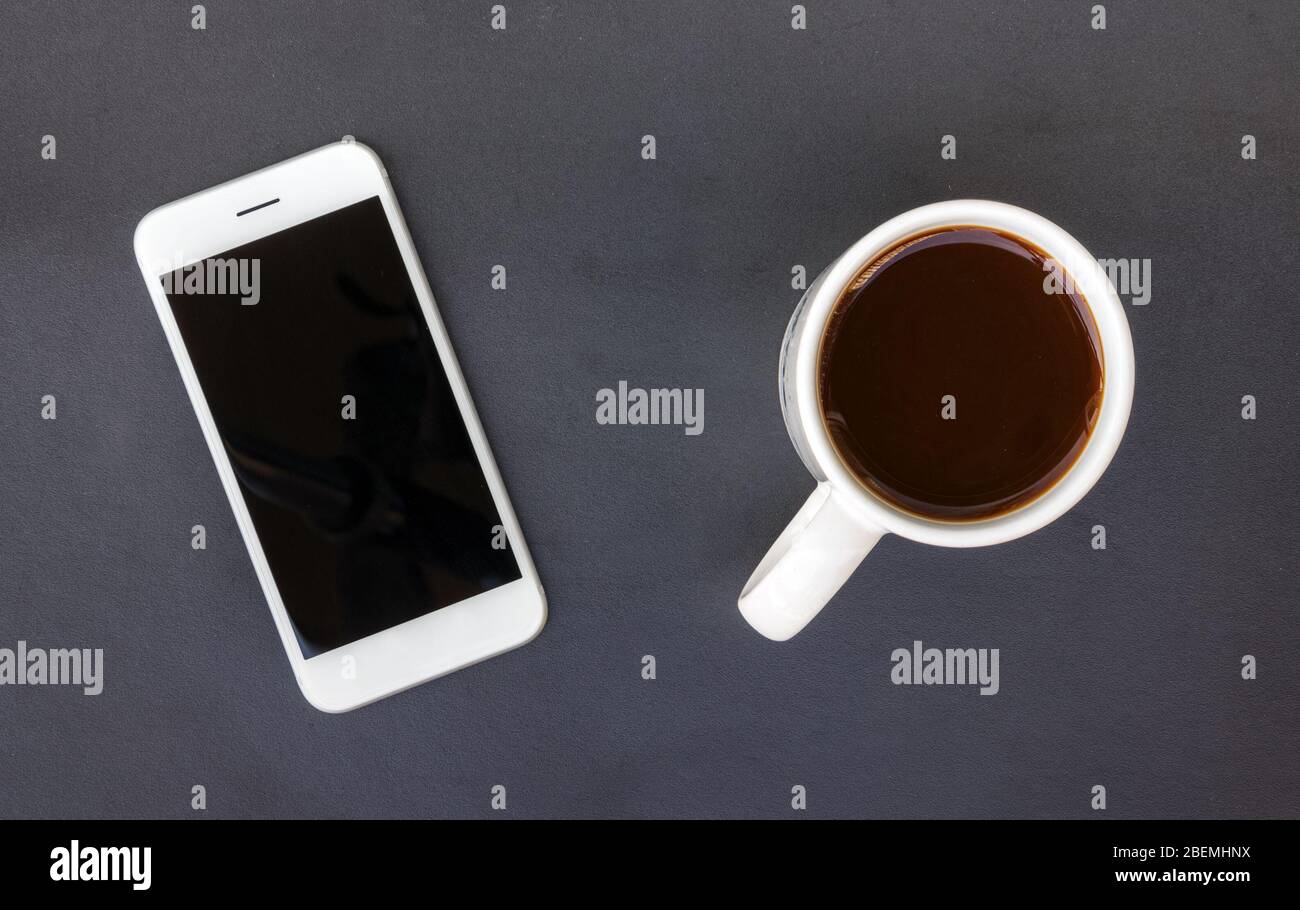 Black table with a white smartphone and a white mug with black coffee. Stock Photo