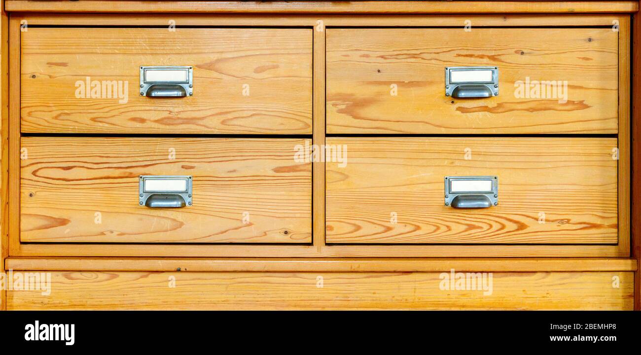 Wooden dresser with four drawers. Drawers with metal handles and small labels. Spruce wood. Frontal view. Stock Photo
