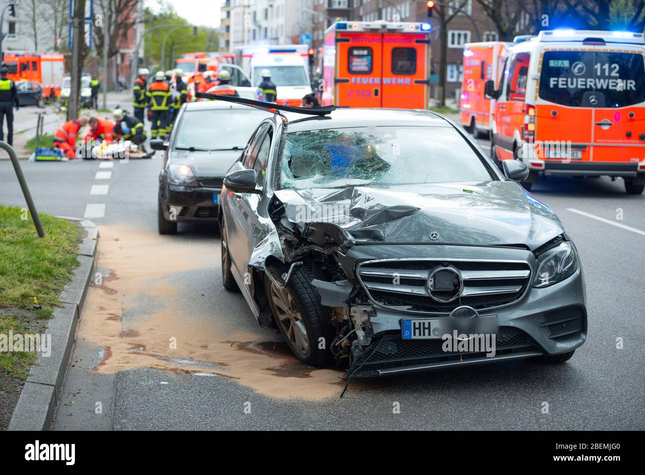 Hamburg, Germany. 14th Apr, 2020. The badly damaged Mercedes is standing on the road after the accident, while rescue workers are caring for the victims in the background. The vehicle had veered off the road in the Altona district, skidded into a traffic light and hit two people. The man and woman suffered life-threatening injuries. The driver was 'apparently' intoxicated, according to a spokeswoman for the Hamburg Police Situation Center. Credit: Jonas Walzberg/dpa - ATTENTION: The license plate was pixelated for legal reasons/dpa/Alamy Live News Stock Photo