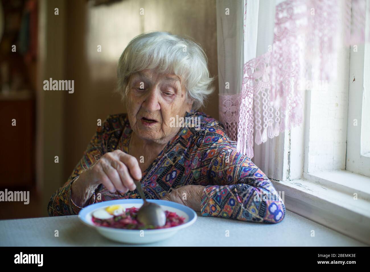 An Old woman eating soup sitting at a table in the her house. Stock Photo