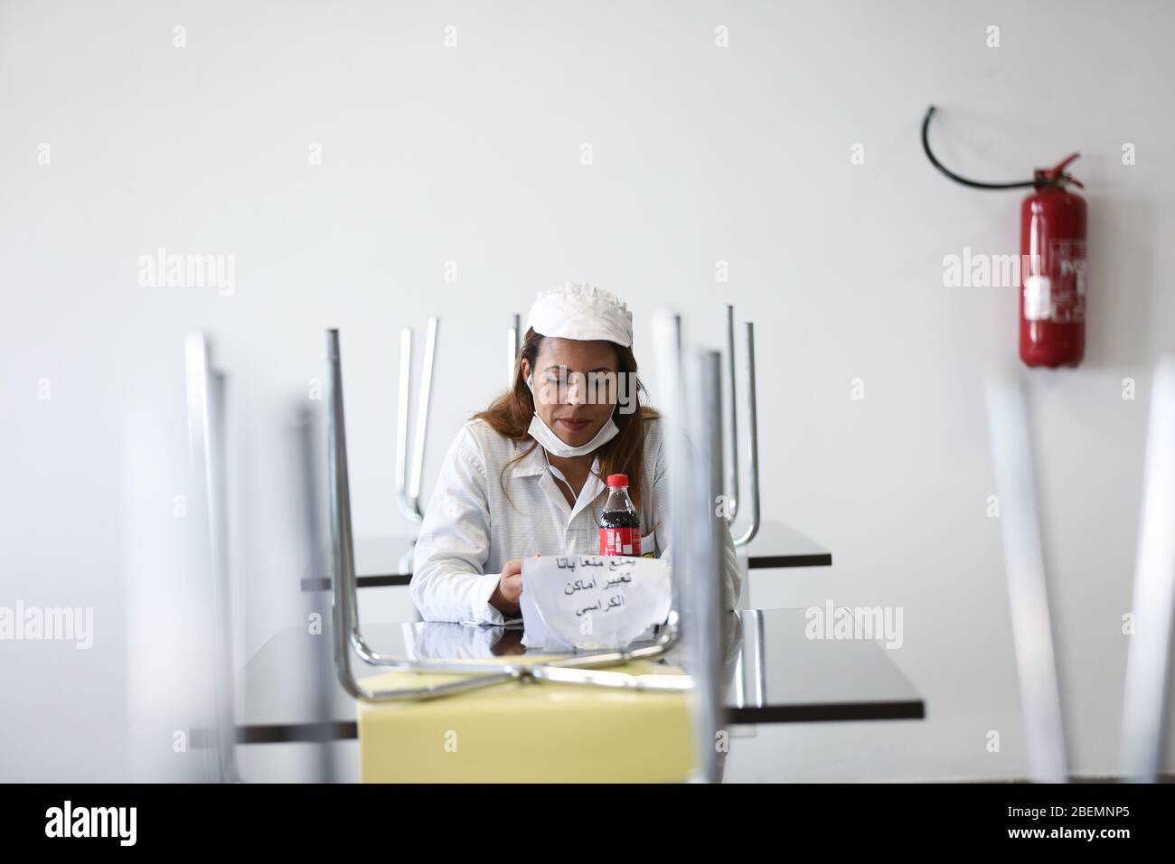 A female factory worker during her fast sits at a table with a note that says 'please dont change chairs places' on Apr. 14, 2020 in Industrial Zone Agba, Manouba, Tunisia. After the announcement of total containment throughout Tunisia on March 22, 2020, factories and viral sectors are continuing their activities while respecting the precautions against the pandemic of CoViD-19. This story follows the daily routine of workers at Marquardt Tunisia automotive factory in Manouba, Tunisia during the Covid-19 coronavirus pandemic. (Photo by Mohamed Krit/Sipa USA) Stock Photo