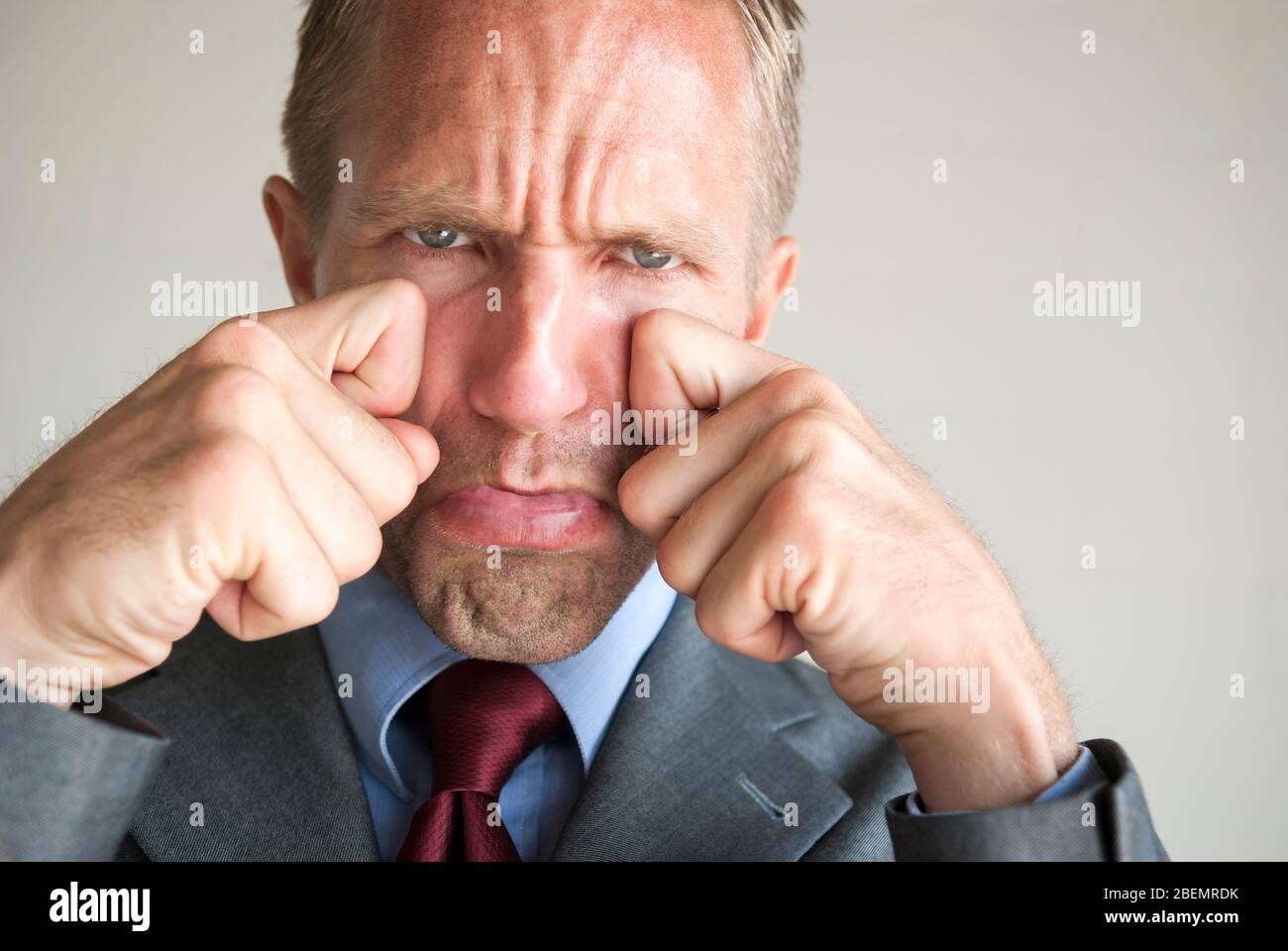Pouting businessman pretending to wipe tears from his cheeks with an exaggerated sad expression Stock Photo
