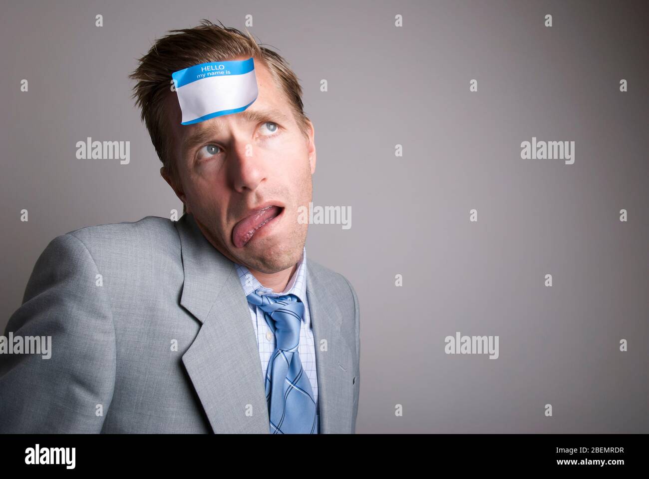 Confused businessman trying to figure out what to put on the blank name tag sticker on his forehead Stock Photo