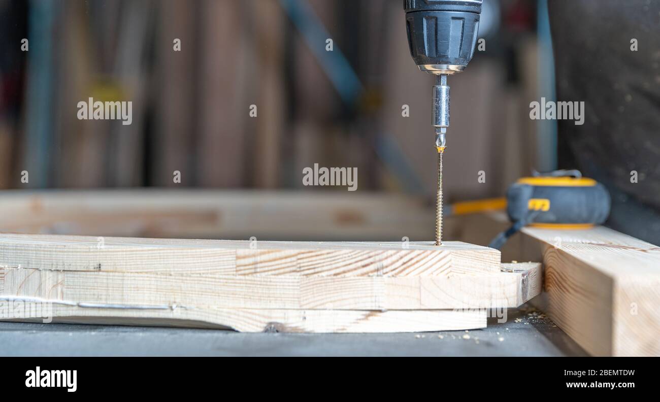 screwing wooden furniture in a joinery using an electric drill bit Stock Photo