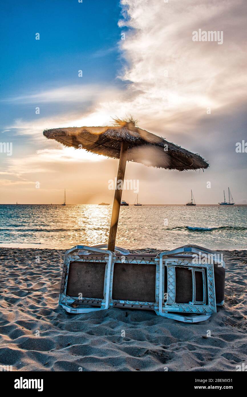 Ses Illetes beach, Formentera, Balearic Islands, Spain. Vertical photo against sun of an umbrella and sunbed on the beach at sunset, with a clouds. Stock Photo