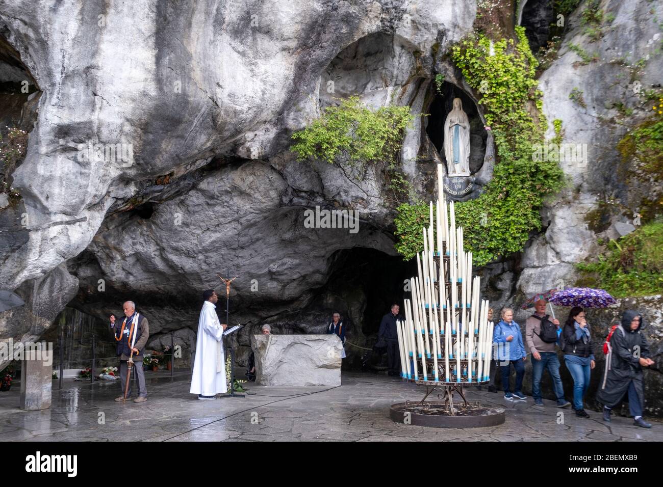 Pilgrims visiting the Massabielle Grotto while a catholic priest celebrates mass in Lourdes, France, Europe Stock Photo