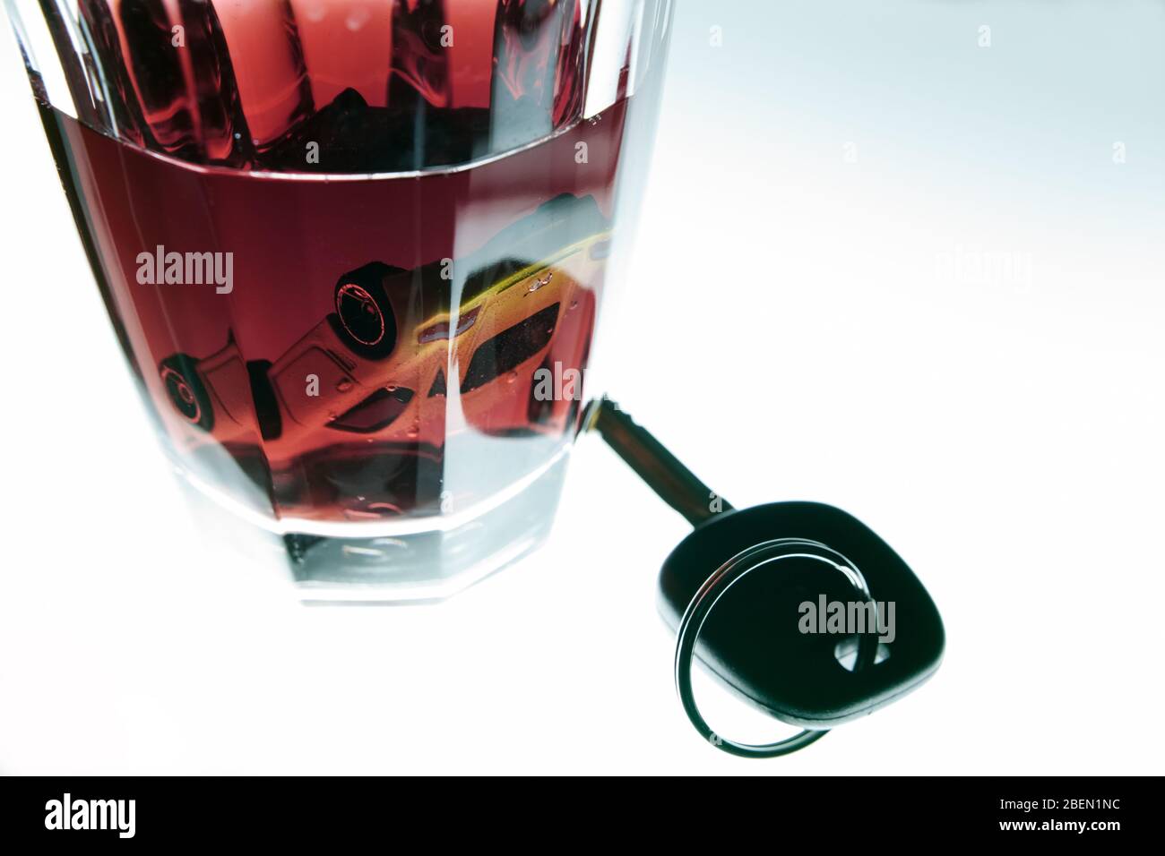 Luminescent table, a little model car drowned upside down in a glass reddish of beverage. Actual car key next to it.. Copy-space. Stock Photo