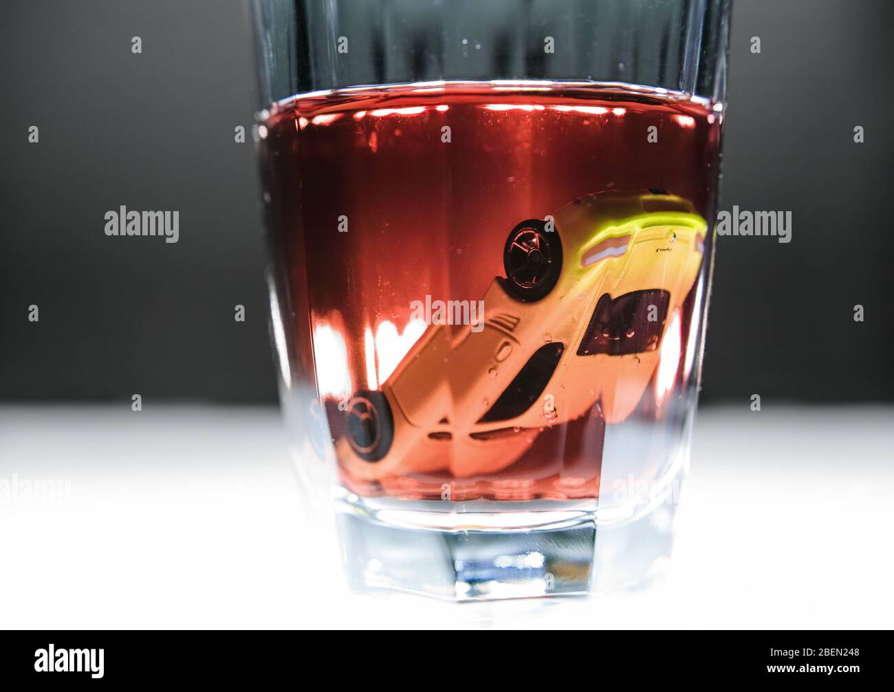 Luminescent table, a little model car drowned upside down in a glass reddish of beverage. Copy-space. Stock Photo