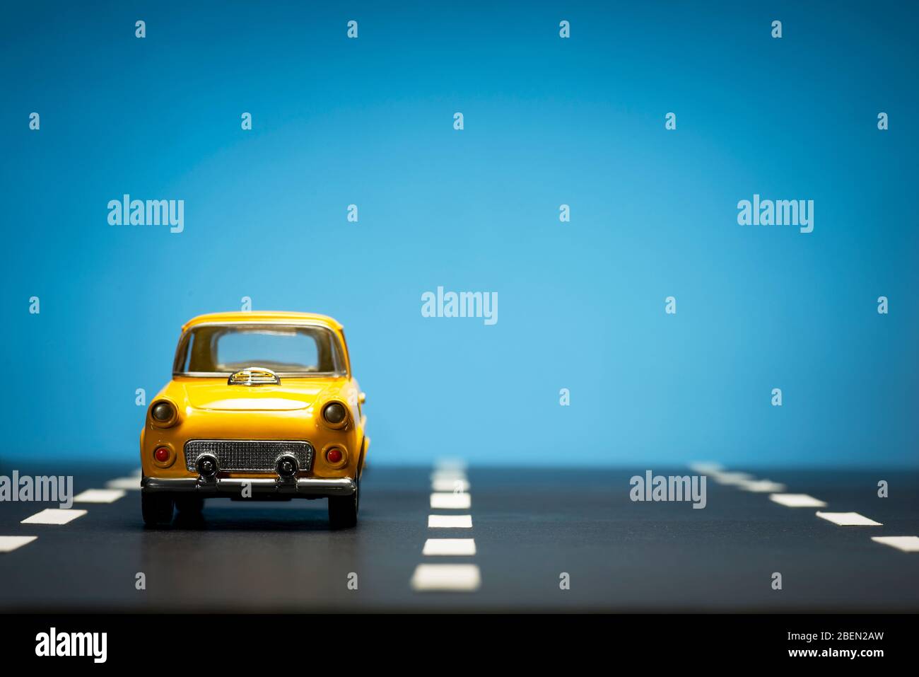 Front view of a Yellow toy car on a blue background and on an asphalt ...
