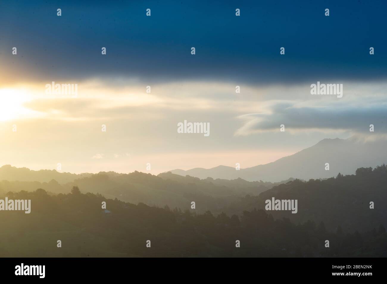 A Soft Sunrise Spreads Paints Pastel Clouds Against a Mountain Vista Stock Photo