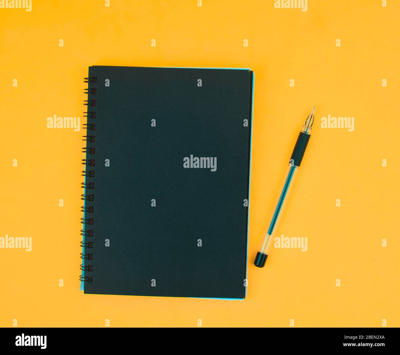 A black ball point pen placed beside a black colored paper diary on an orange paper background Stock Photo