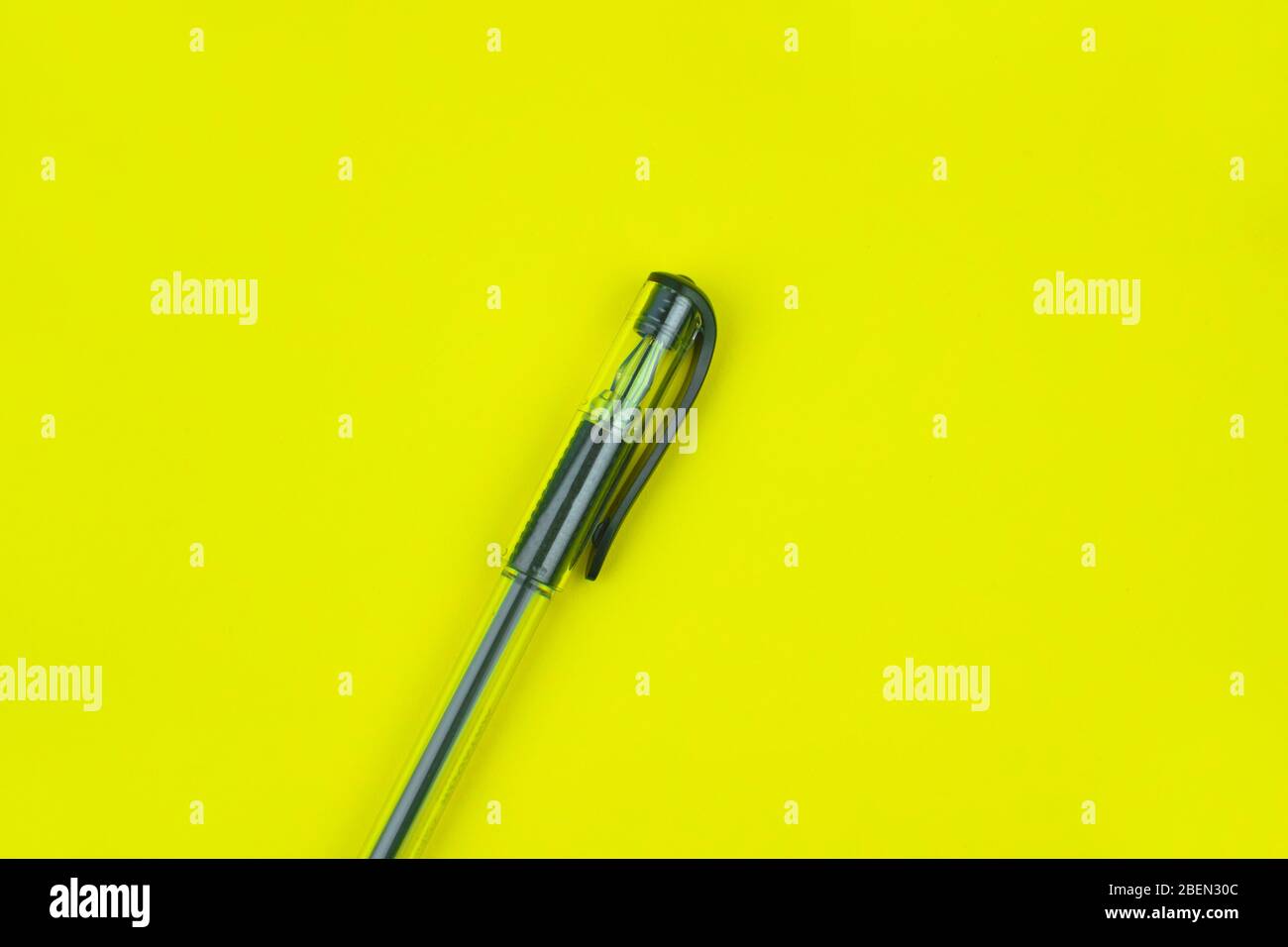Black colored ball point pen placed over a bright yellow colored empty paper background Stock Photo
