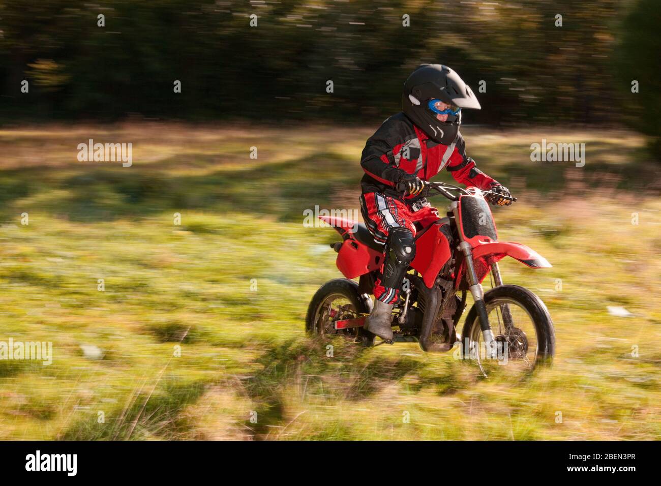 12 year old boy riding his motocross motorcycle through field Stock Photo