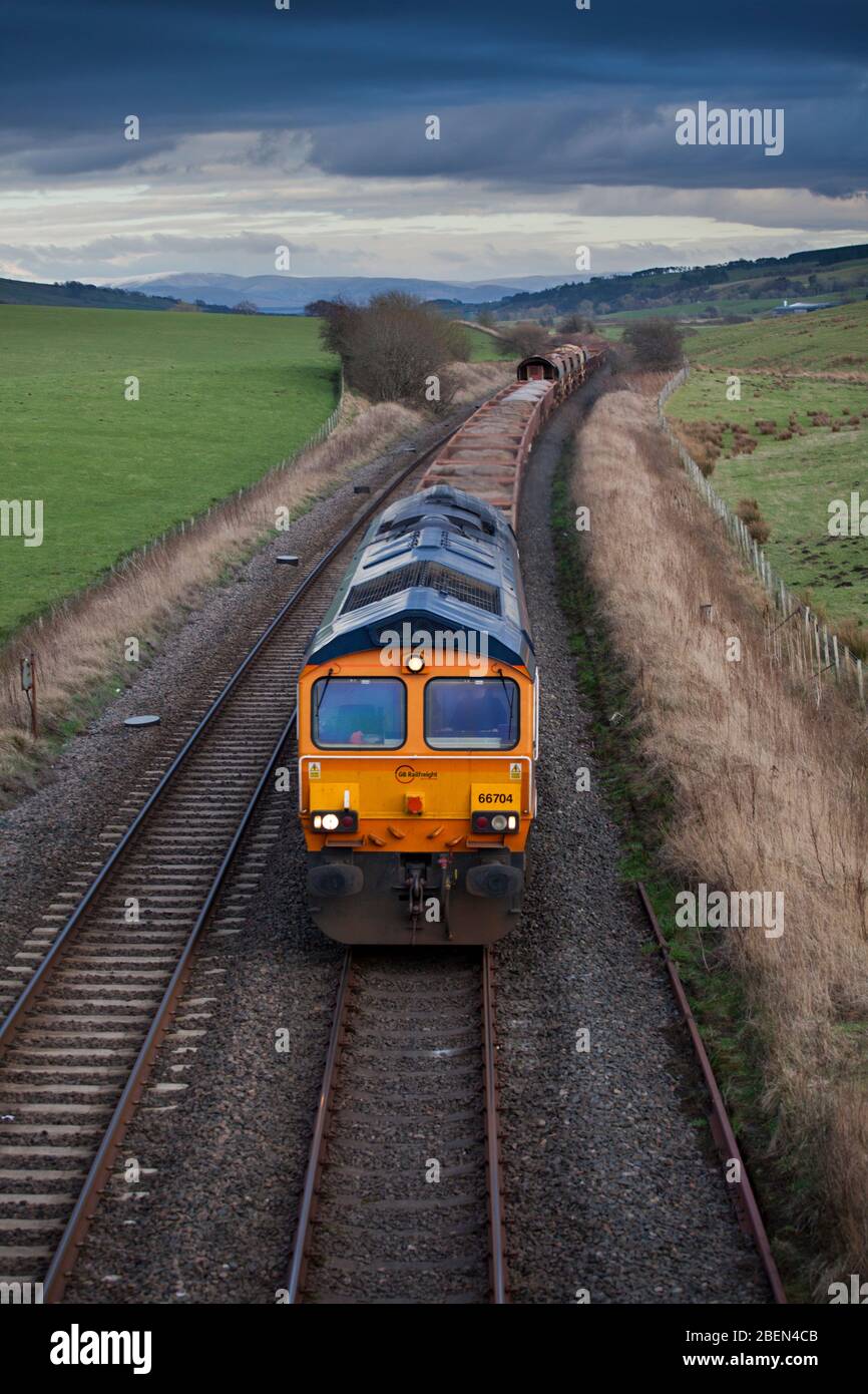 GB Railfreight class 66 locomotive 66704 passing New Cumnock, south west Scotland with a freight train carrying materials for Network Rail. Stock Photo