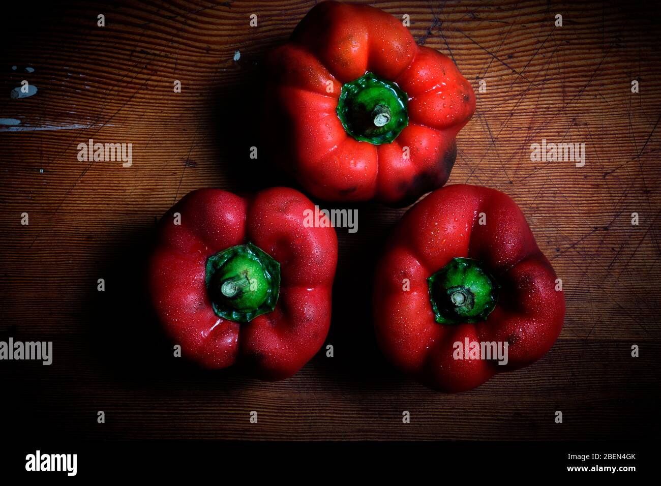 Three fresh red peppers with water drops on a wood table Stock Photo