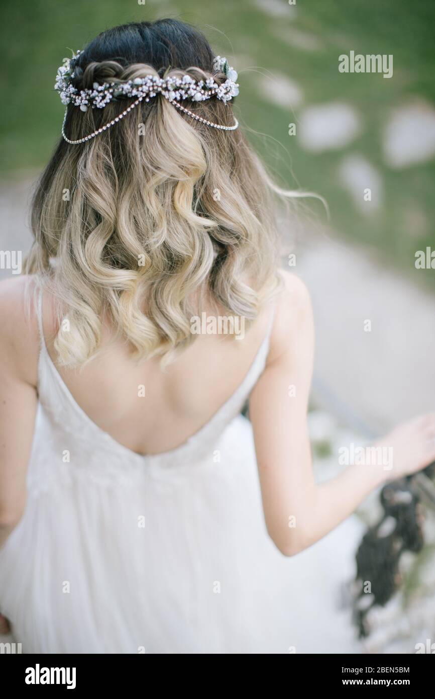 The bride poses showing her back. As the sun goes down, at the wedding venue. The bride is holding a bridal flower in her hand. / Skirts of the bride. Stock Photo