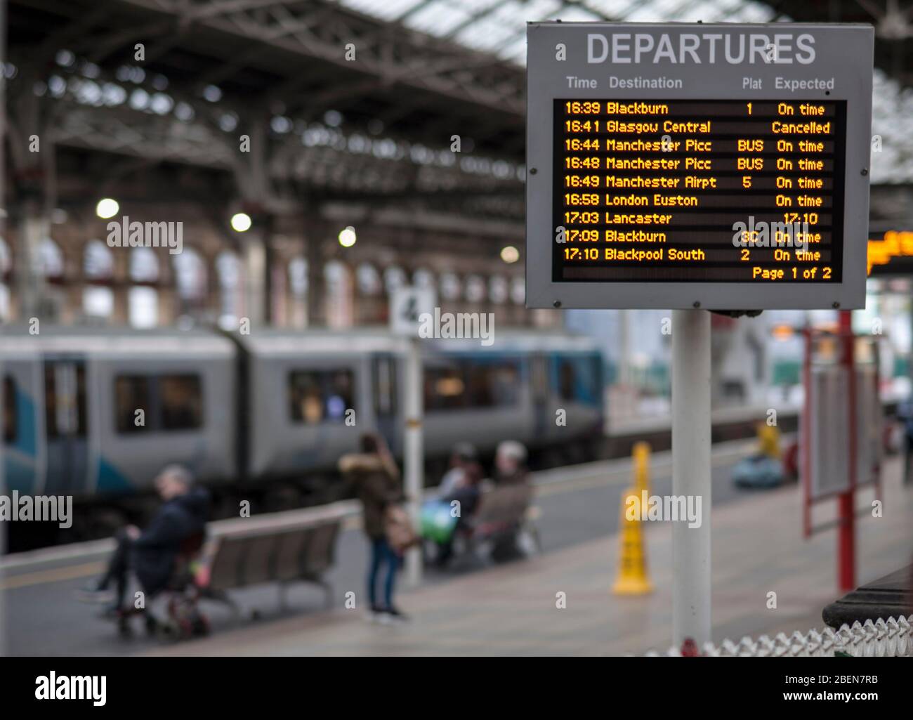 Departure screen at Preston railway station showing on time, delayed cancelled trains , rail replacement buses with passengers and a train. Stock Photo