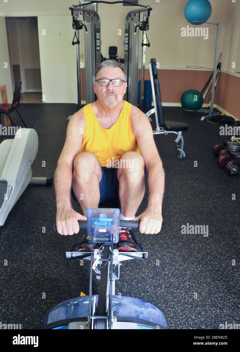 A senior citizen uses a rowing machine in the gym Stock Photo