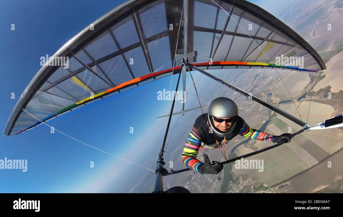 Smiling hang glider pilot shows thumb up while flyingh high above ground on his colorful wing Stock Photo