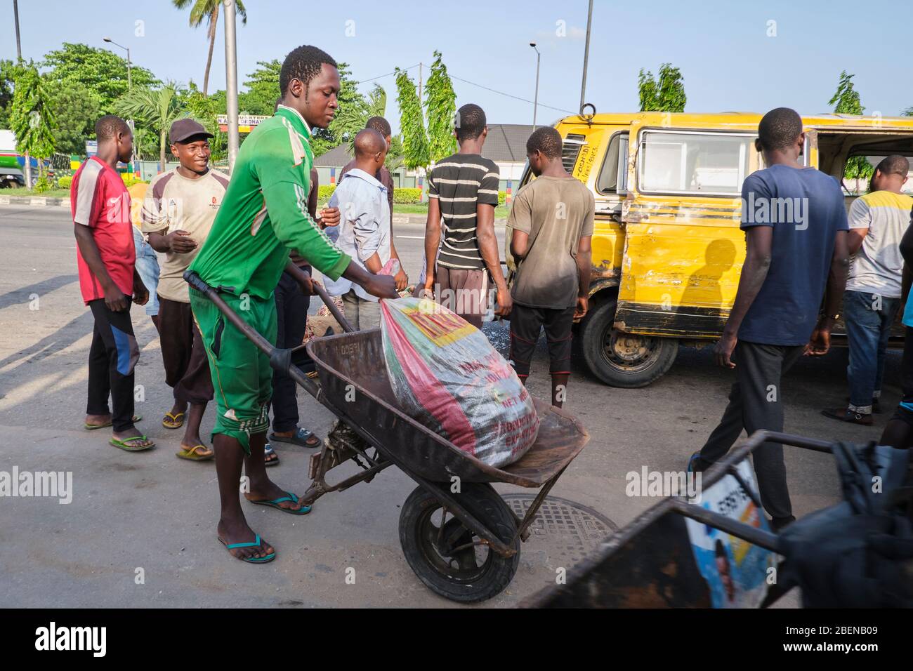 A wheelbarrow pusher lifts a bag into his wheelbarrow shortly after a bus dropped people returning from the market. Stock Photo