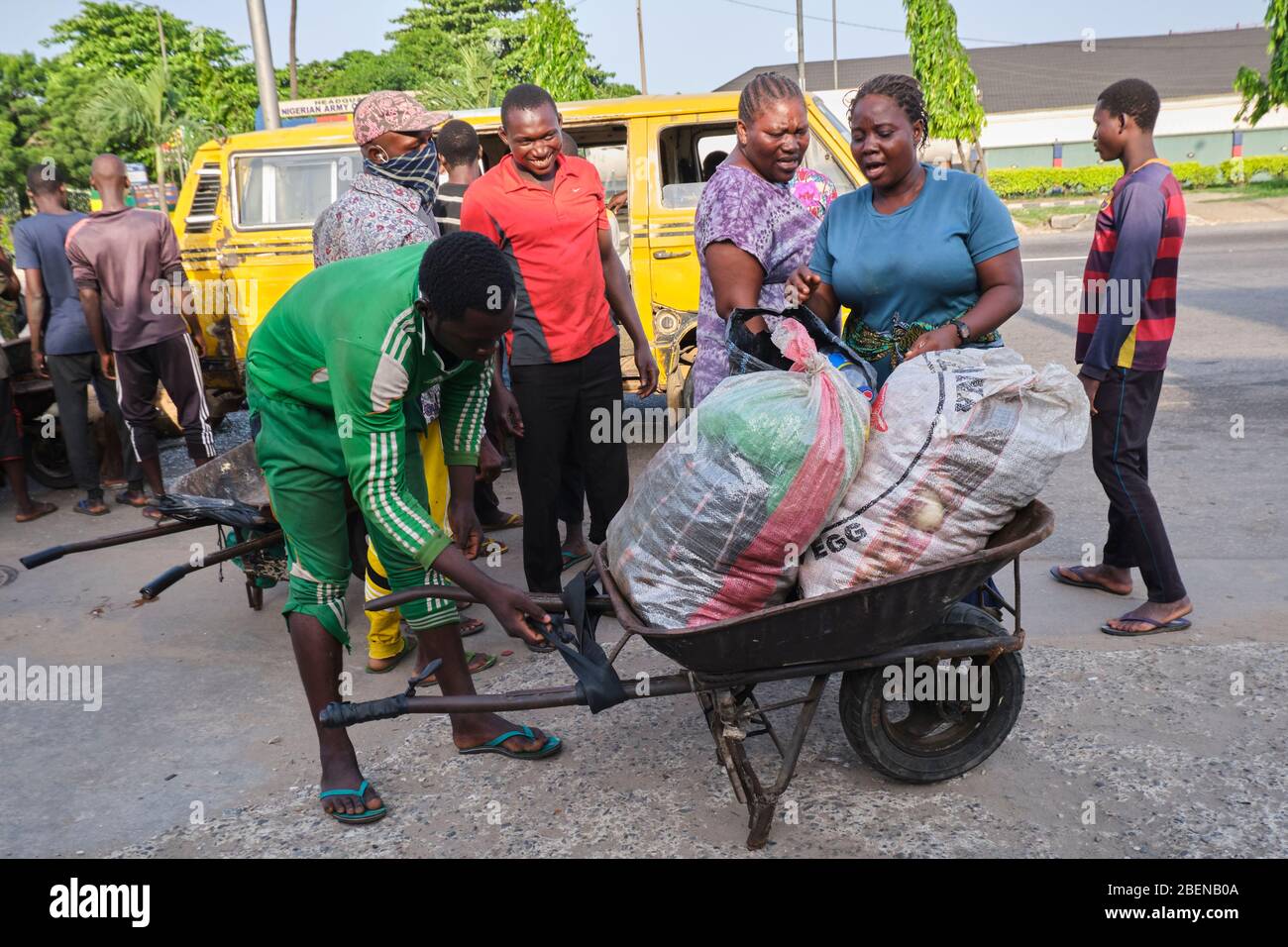 A wheelbarrow pusher loads bags of goods into his wheelbarrow shortly after a bus dropped a few people returning from the market. Stock Photo