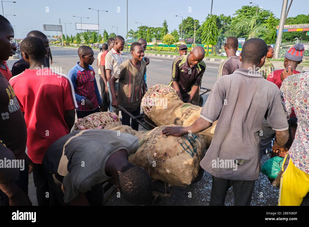 A group of wheelbarrow pushers load bags of onions into their wheelbarrow at a bus stop in Lagos, Nigeria. Stock Photo