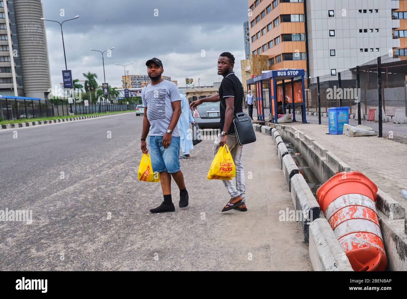 Two guys look out for vehicles at a bus stop after shopping at a nearby supermarket during Covid-19 lockdown in Lagos, Nigeria. Stock Photo
