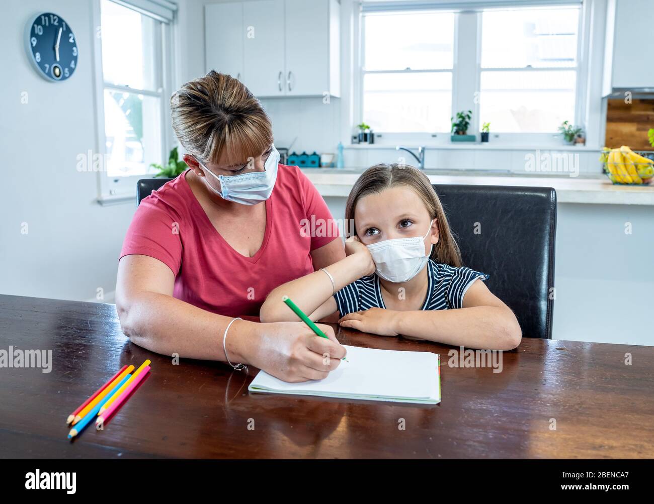 Coronavirus Outbreak. Lockdown and school closures. Mother helping bored daughter with face mask studying online classes at home. COVID-19 pandemic fo Stock Photo