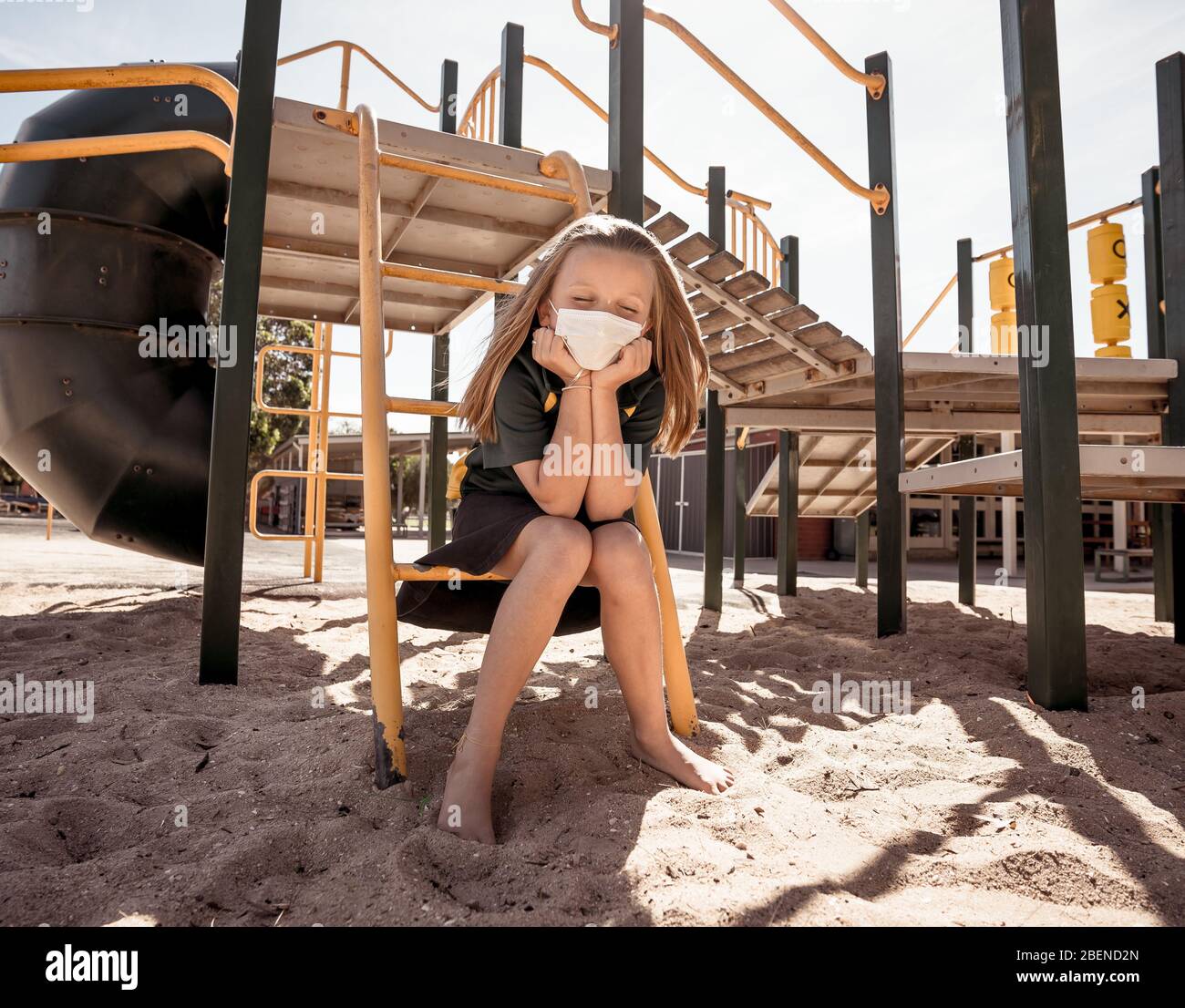 Covid-19 outbreak schools closures. Sad Schoolgirl with face mask bored feeling depressed and lonely in empty playground as school is closed. Restrict Stock Photo