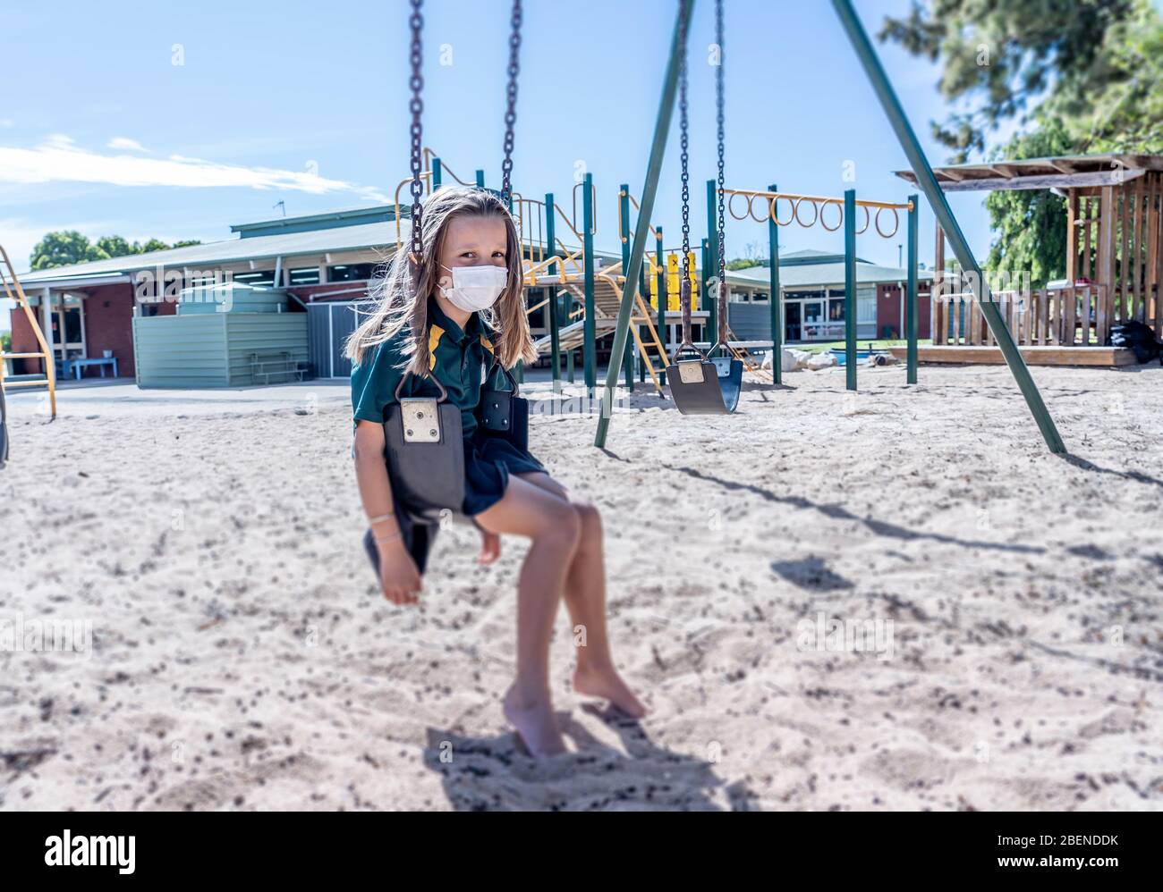 Covid-19 outbreak schools closures. Sad Schoolgirl with face mask bored feeling depressed and lonely in empty playground as school is closed. Restrict Stock Photo