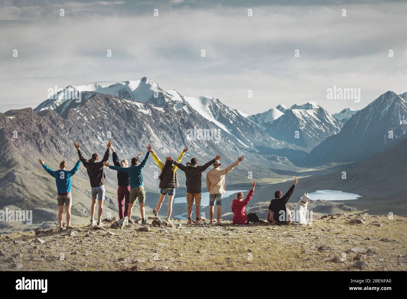 Big group of happy young hikers are standing with raised arms in mountains Stock Photo