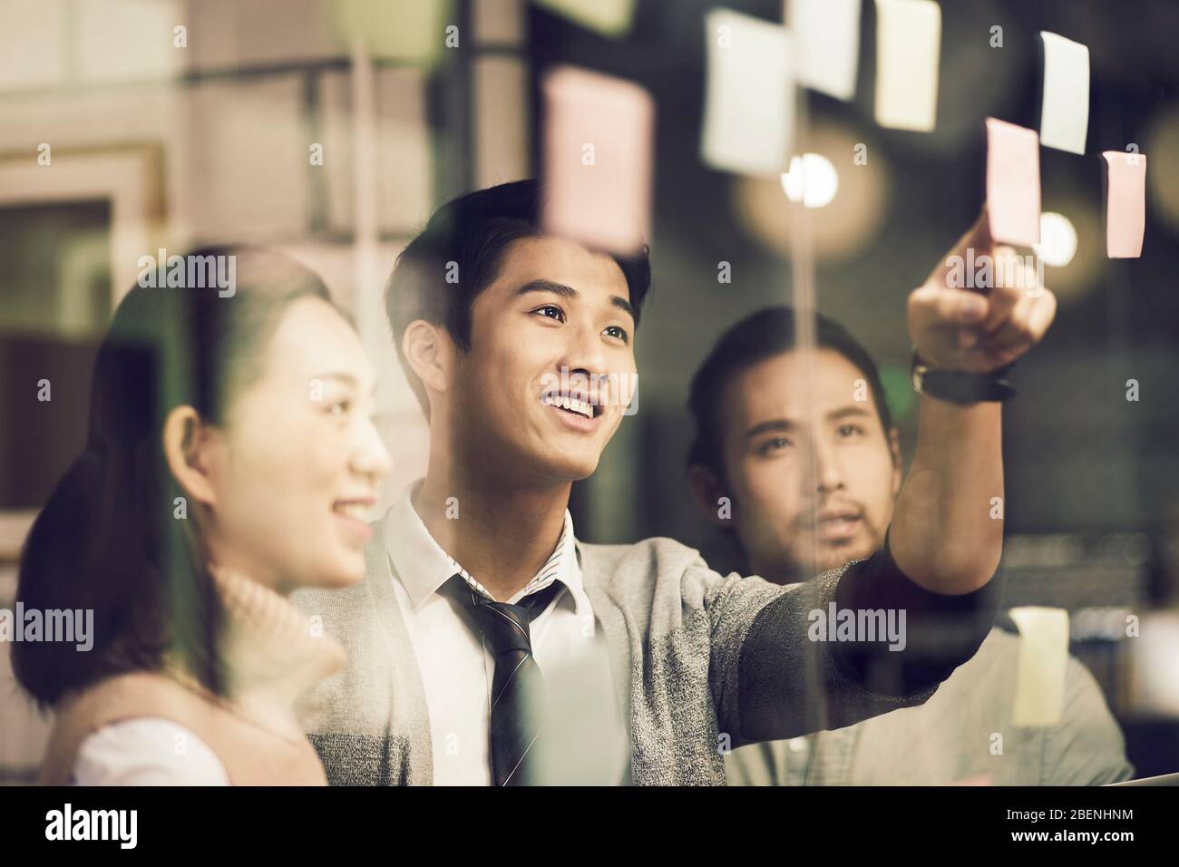 three asian small company businesspeople young entrepreneurs meeing discussing in office using sticky notes Stock Photo