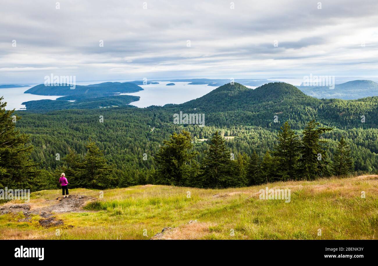 A woman stands in a clearing looking out at the view  half way up Mount Constitution in Moran State Park, Orcas Island, Washington, USA. Stock Photo