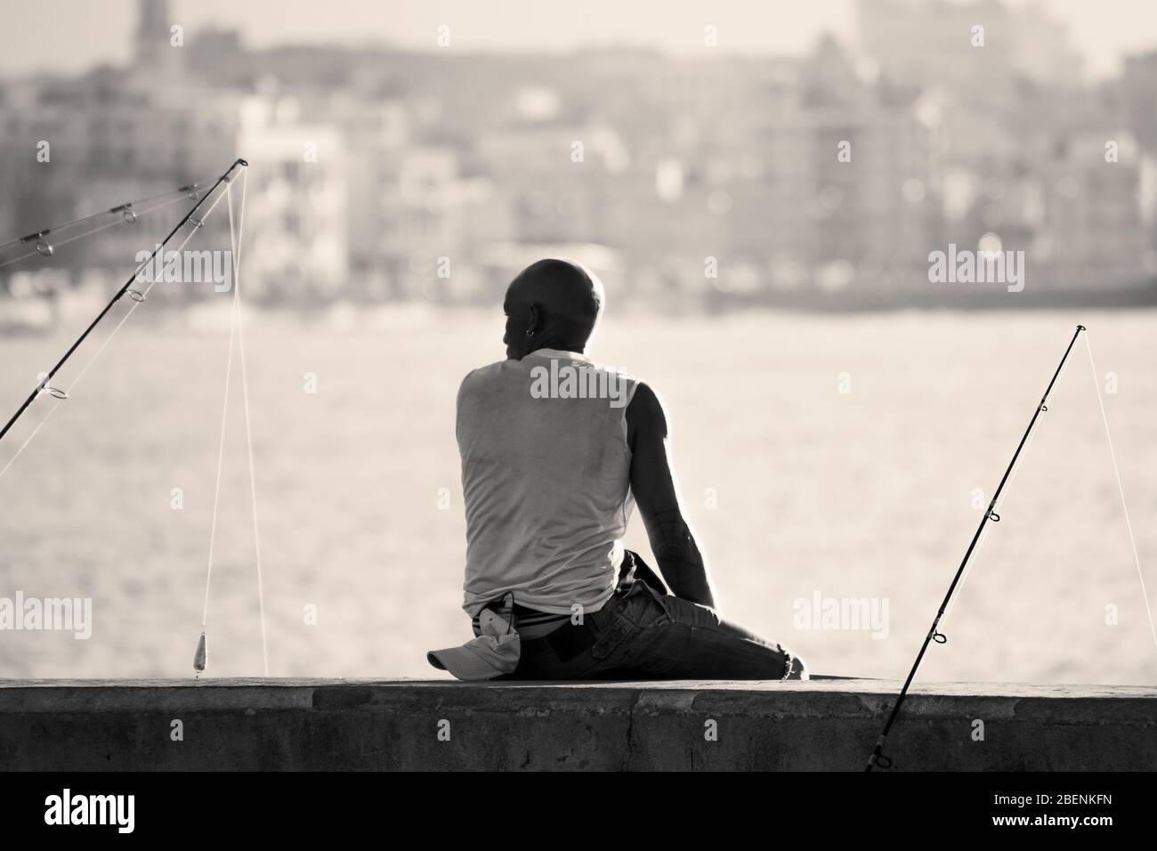 A fisherman sits on the ocean wall in Havana (Cuba) which runs along the side of the Malecon highway seen in August 2014. Stock Photo