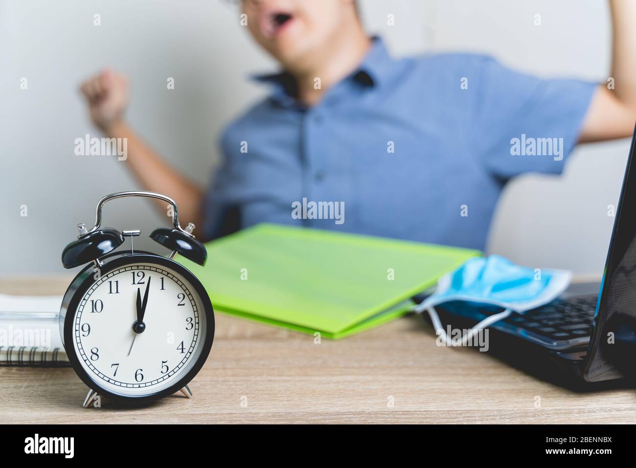 Work from home during the outbreak of the virus. Alarm Clock on the table at midnight with blur the businessman works from home and He's stretchonesel Stock Photo