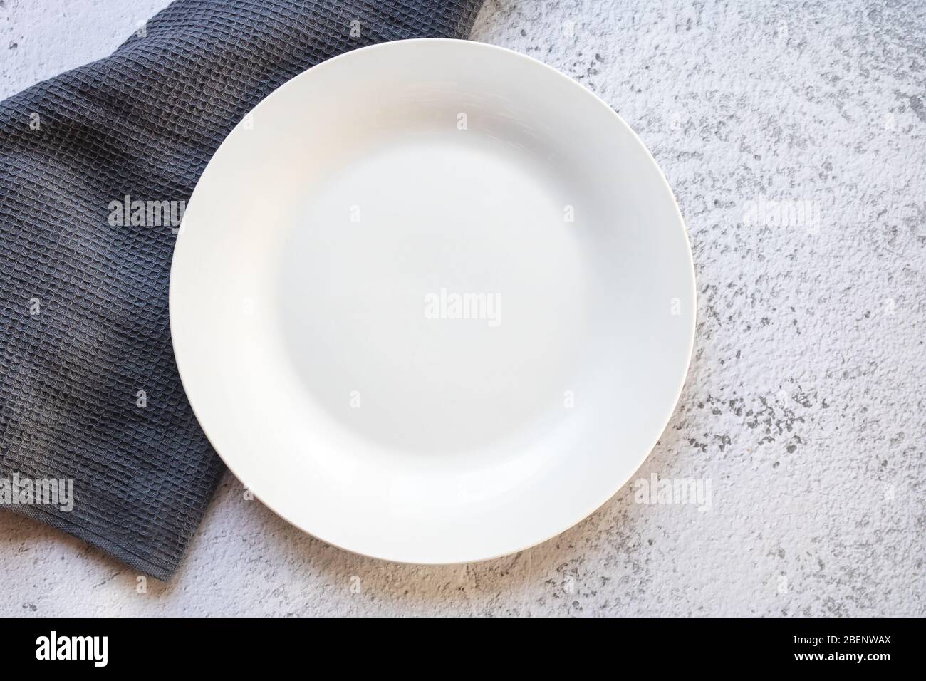 Empty white plate next to a gray kitchen towel Stock Photo