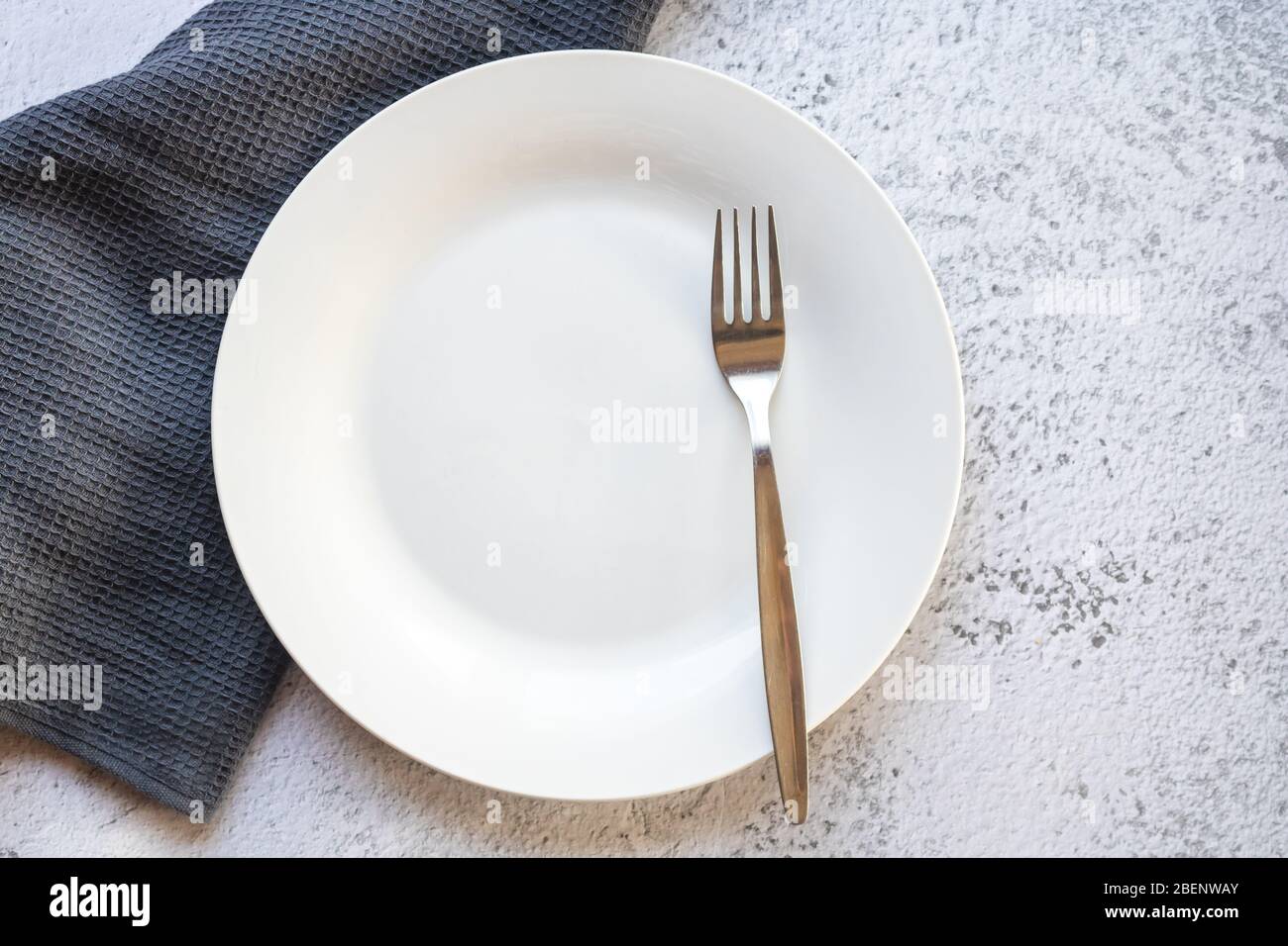 Empty white plate next to a gray kitchen towel Stock Photo