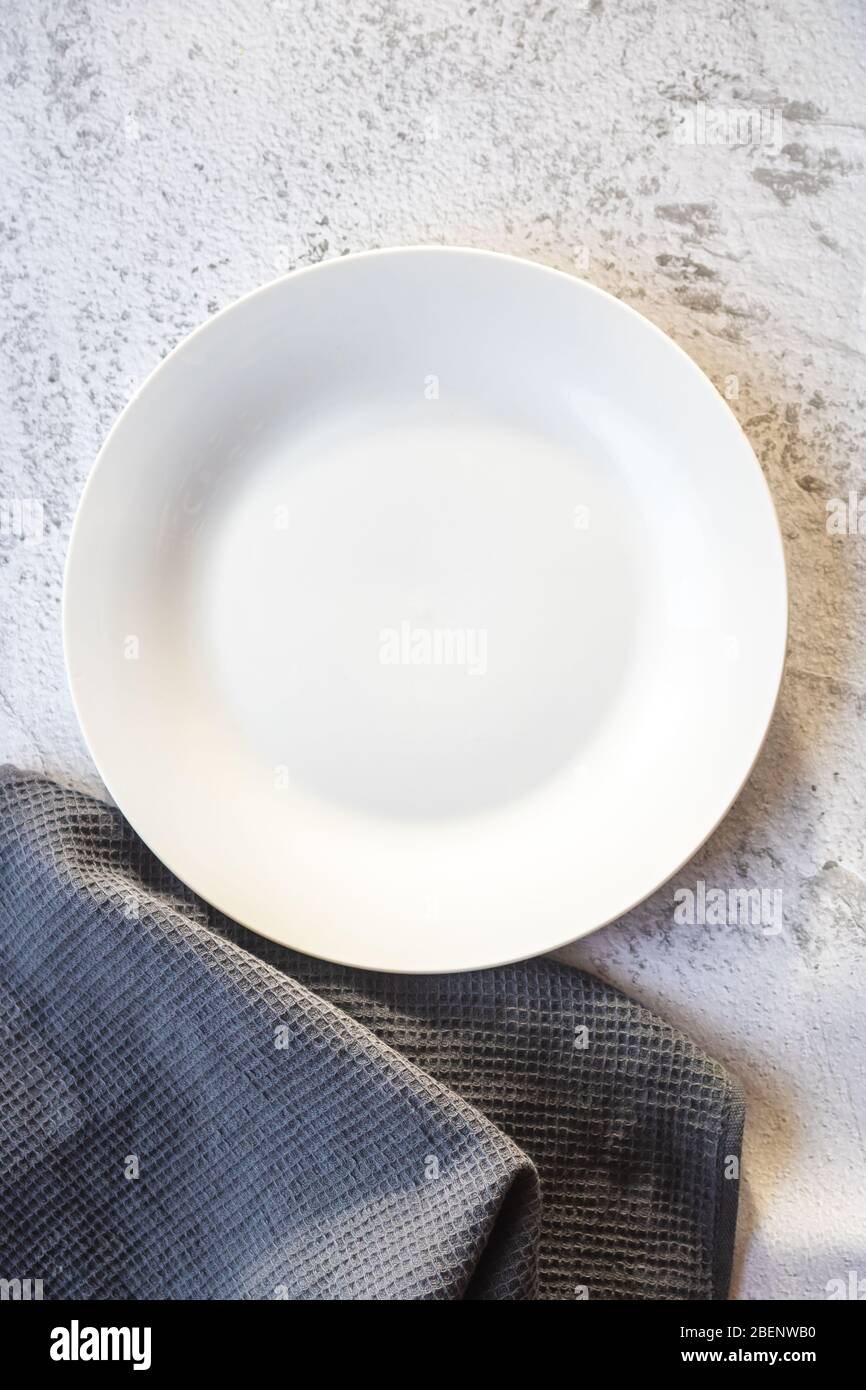 Empty white plate next to a gray kitchen towel Stock Photo